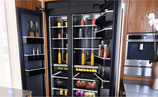 Un réfrigérateur JennAir ouvert dans une cuisine avec un four mural JennAir. À l’intérieur se trouvent des boissons et des aliments comme des citrons, des petits fruits et des choux. Un réfrigérateur JennAir ouvert dans une cuisine avec un four mural JennAir. À l’intérieur se trouvent des boissons et des aliments comme des citrons, des petits fruits et des choux.